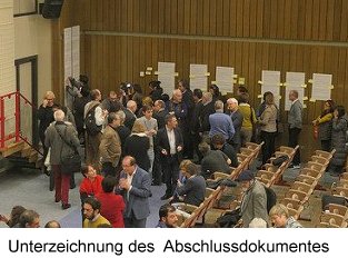 Blick in den Saal. Die Teilnehmer stehen und sitzen im Saal, unterhalten sich.